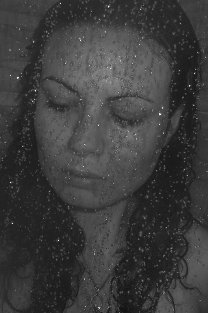 A woman as seen from behind a steamy glass shower screen.