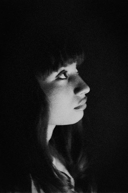 The side profile of a young woman with bangs in the dark looking slightly up.