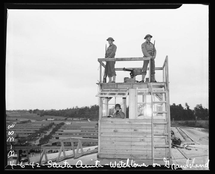 A watchtower with American soldiers looking in the distance over internment camps. 