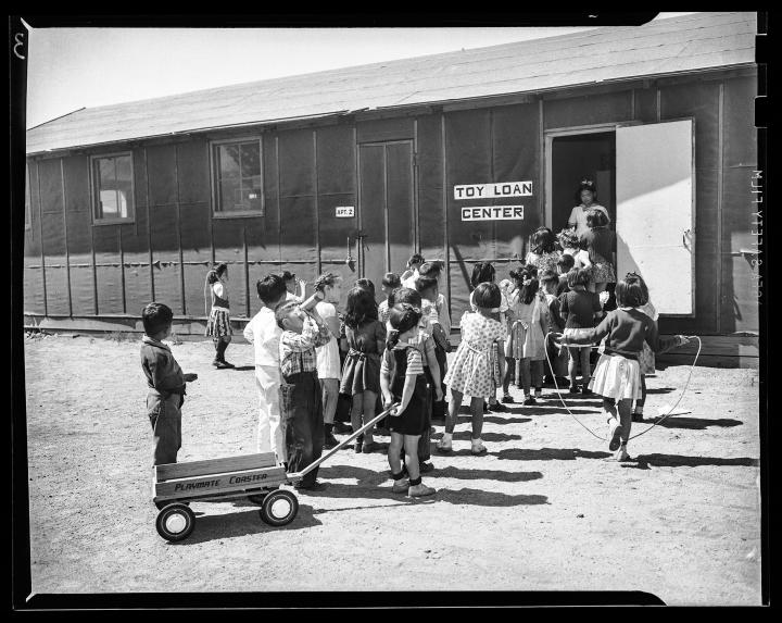 Children lined up outside a makeshift trailer with a sign that reads "Toy Loan Center".