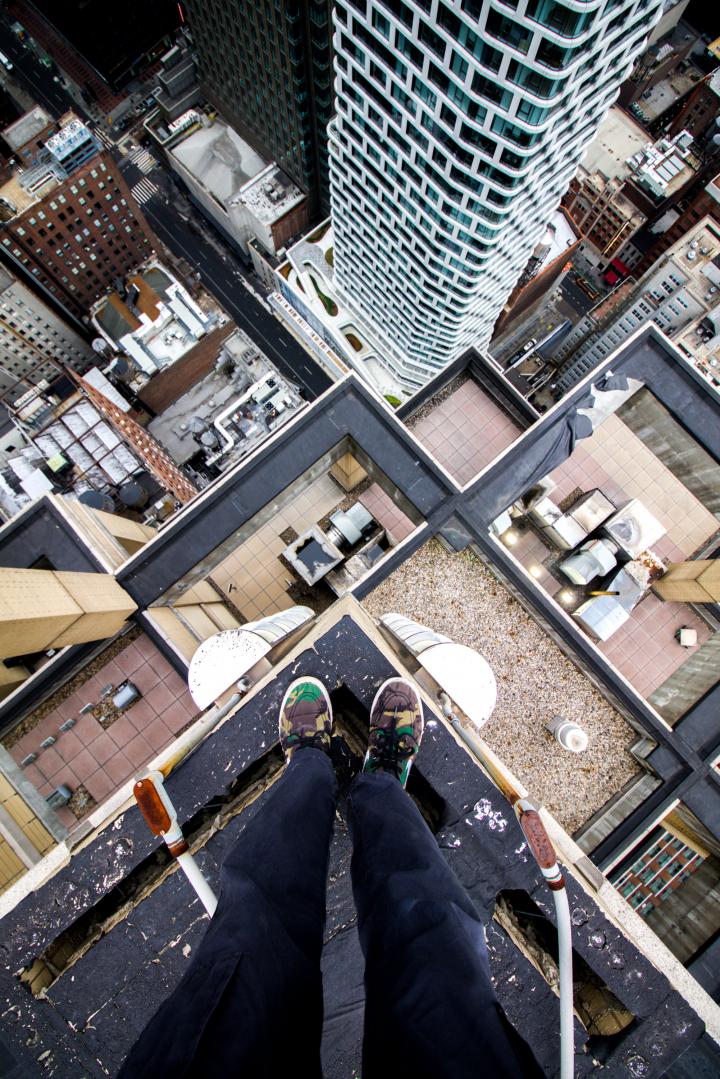 The extreme edge of a skyscraper, observing the surrounding cityscape below.  