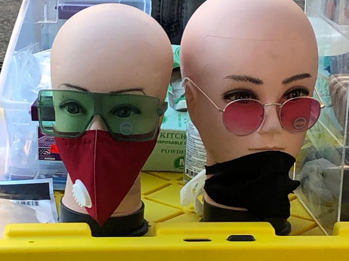 Two bald mannequins wearing COVID 19 masks and sunglasses. 