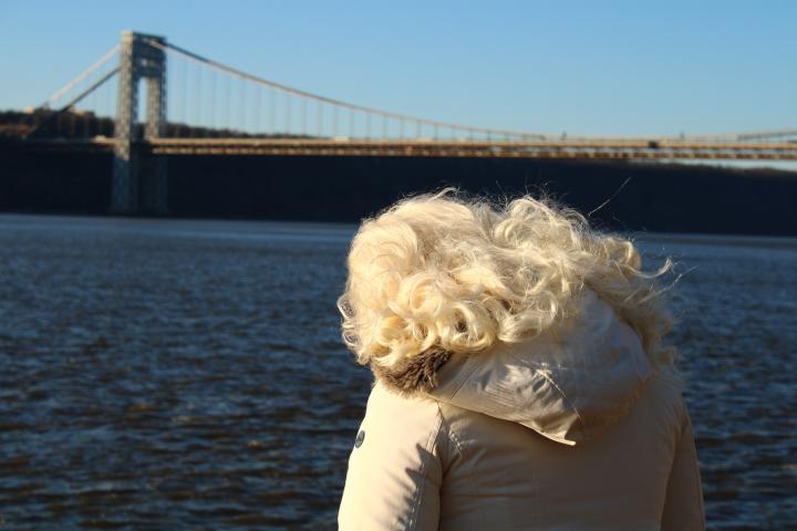 The backside of a blonde woman's head as she looks on to a river. 