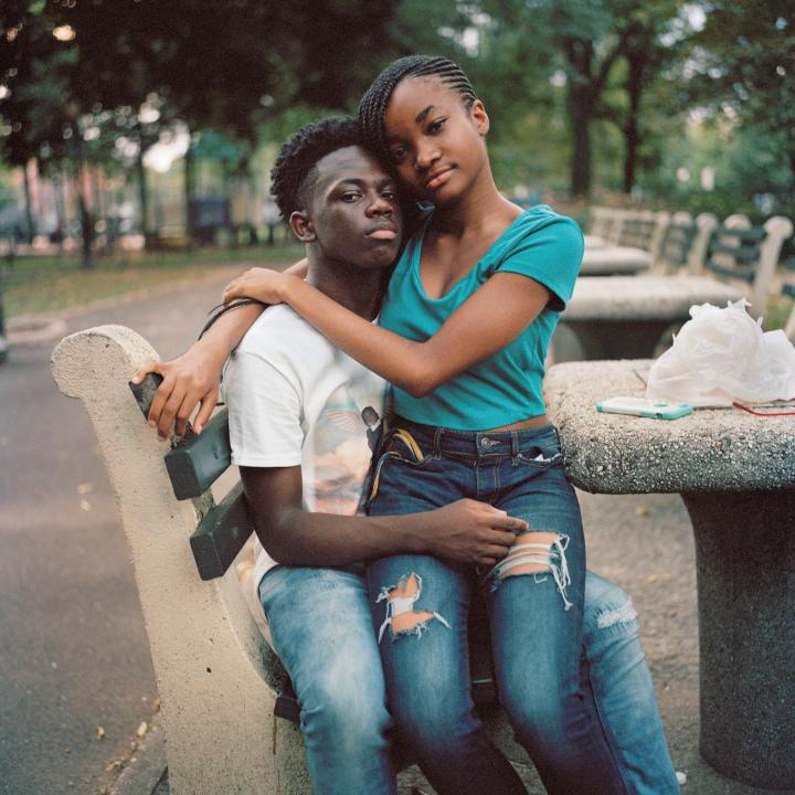A girl sitting on a guys lap in the park