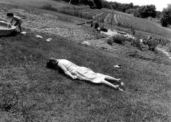 A black and white image of 2 kids outside with the girl facedown on the floor