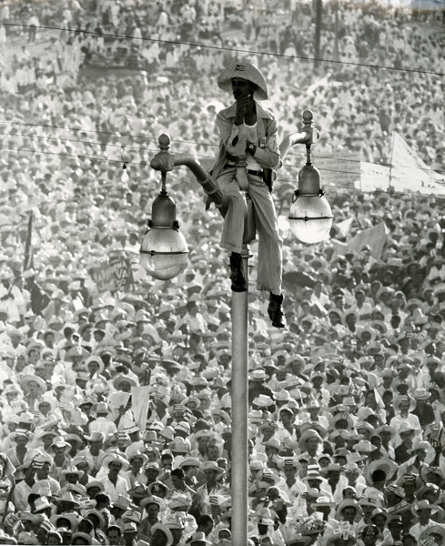 Black and white image of a person sitting on top of a light post